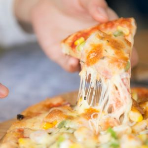 Appetizing close-up of a cheesy pizza slice with toppings, being pulled from a freshly baked pie.